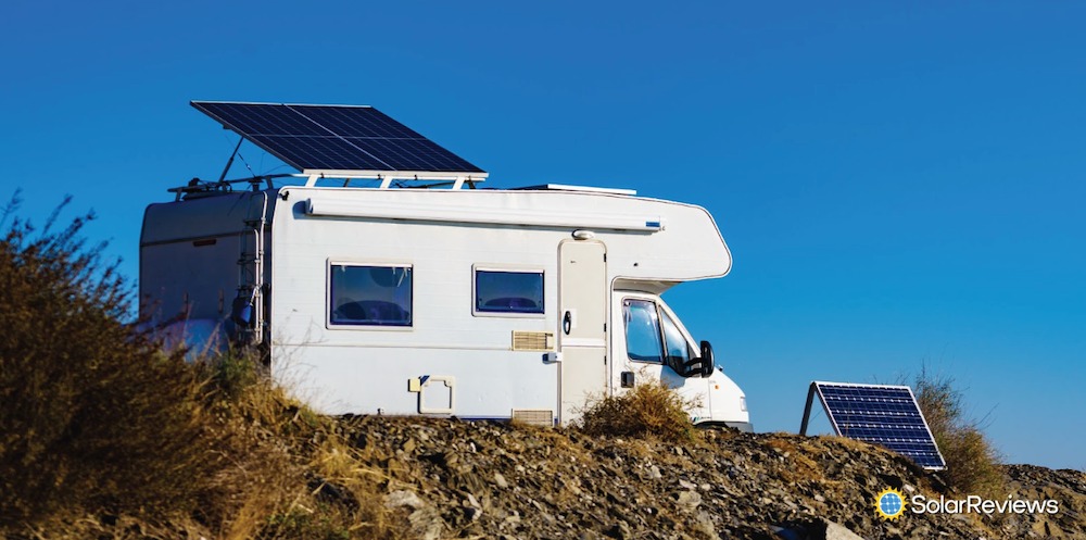 An RV with a solar panel mounted on the roof and a portable solar panel on the ground